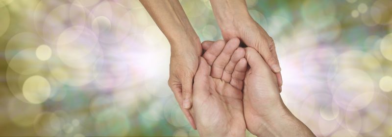 Compassion banner - wide banner with a woman's hands holding a man's cupped hands in a needy gesture on a bokeh and light burst background and plenty of copy space either side